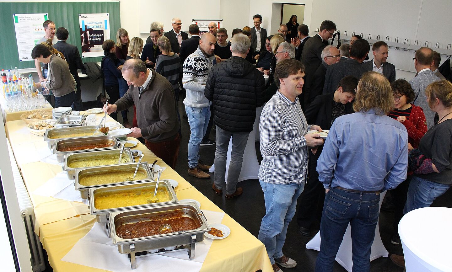 Viele Personen vertieft in Gesprächen neben einem Suppenbuffet.