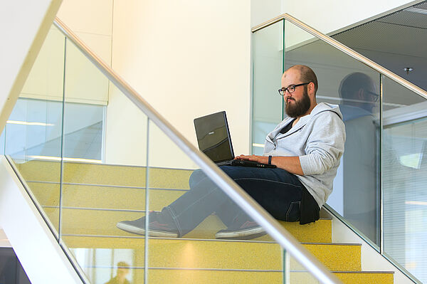 Student mti Laptop sitzt auf gelber Treppe