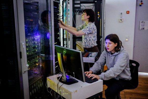 Zwei Personen sitzen in eiem Serverraum und arbeiten.