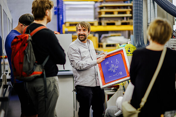 HTWK-Angehöriger zeigt einer Gruppe im Labor eine bunte Tafel