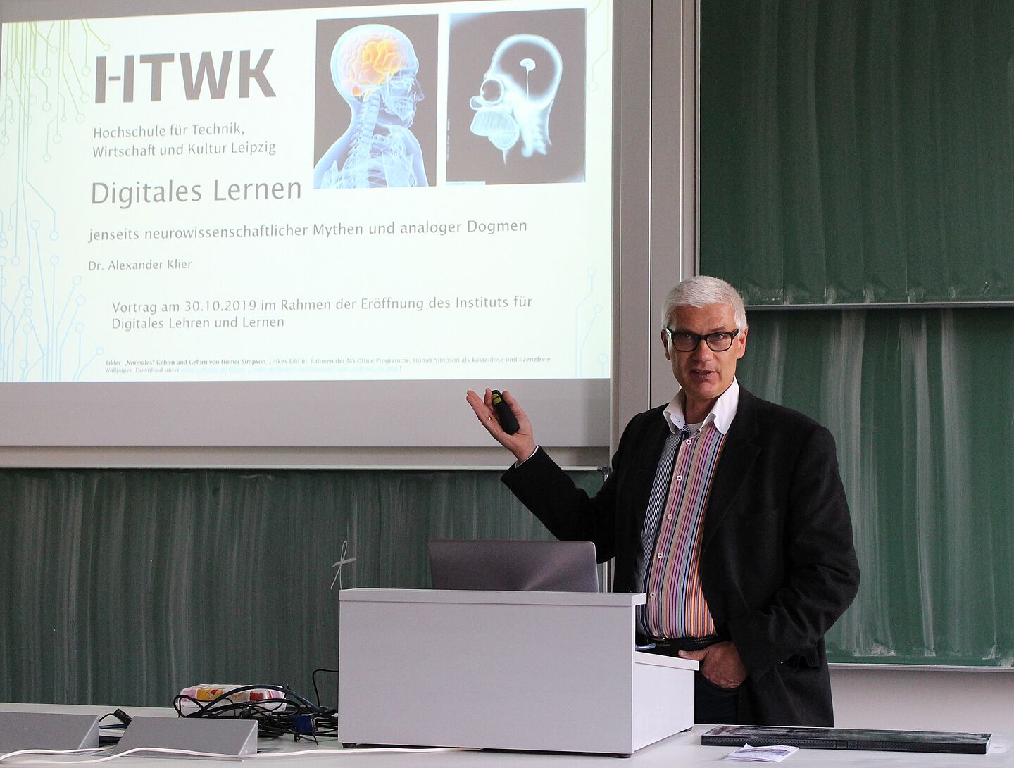 Person steht am Rednerpult zeigt auf Präsentationsfolien.