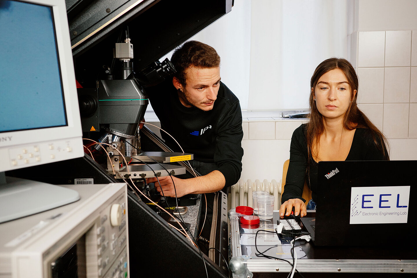 ein Mann und eine Frau messen Transistoren und blicken in einen Computer