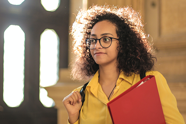 Eine Studentin hält eine Mappe in der Hand und schaut in die Ferne.