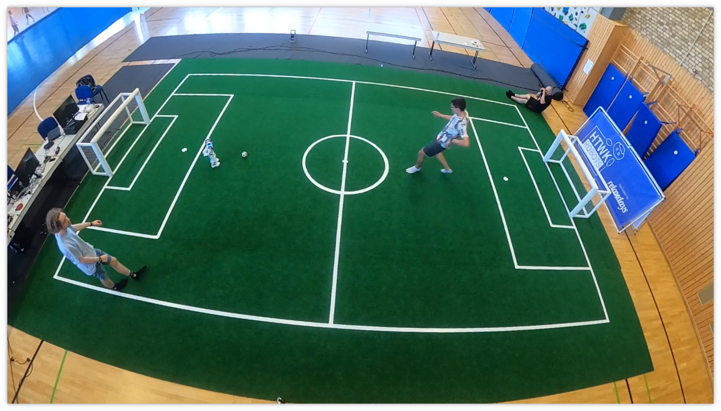 Mensch und Maschine: Vorbereitungen auf die Robocup-WM 2021. (Foto: HTWK Robots) kleines Fußballfeld mit einem Roboter und zwei Menschen