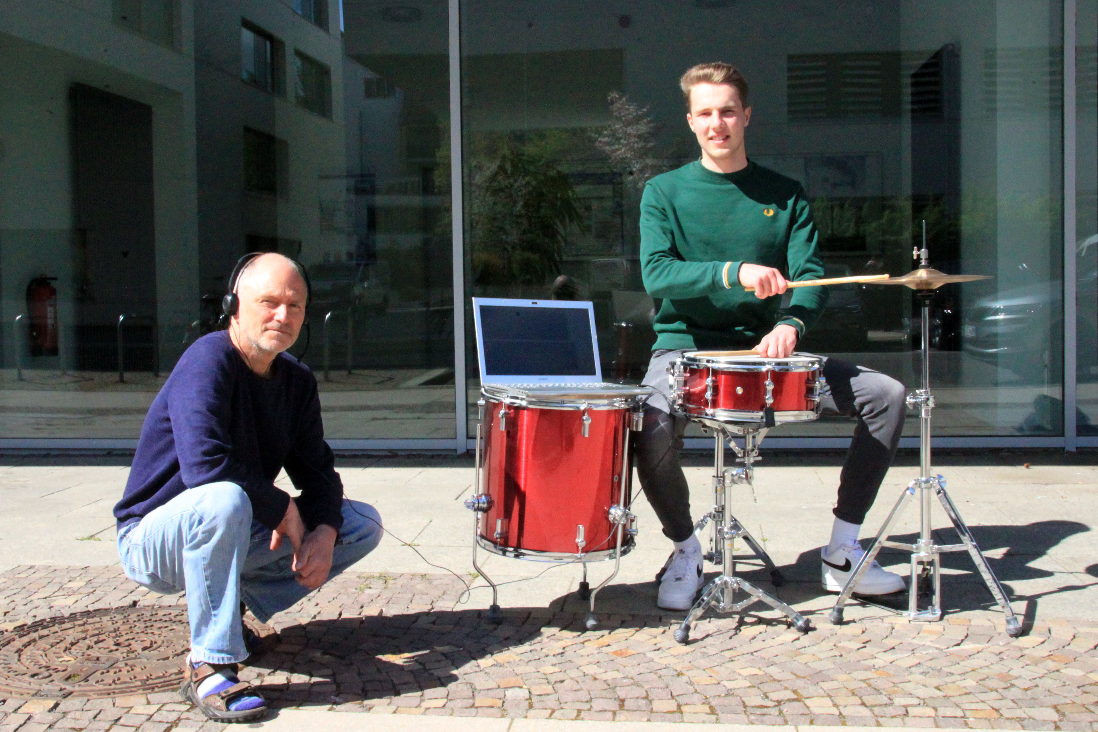 Professor Christian Weickhardt und Florian Wedhorn (v.l., Foto: Marie Nowicki/HTWK Leipzig) In der Sonne steht ein rotes Schlagzeug, daran sitzt Florian Wedhorn und hält die Schlagzeugstöcke auf die Trommeln; auf einer der Trommeln steht ein Laptop und daneben hockt Professor Christian Weickhardt mit Kopfhörern